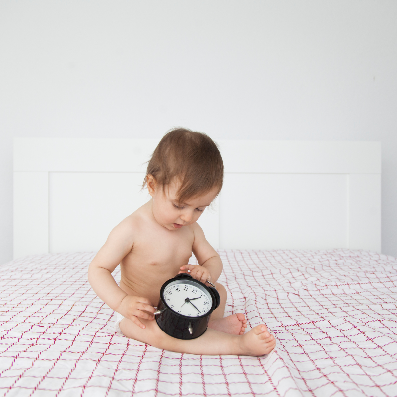 Toddler sitting on bed looking at a clock