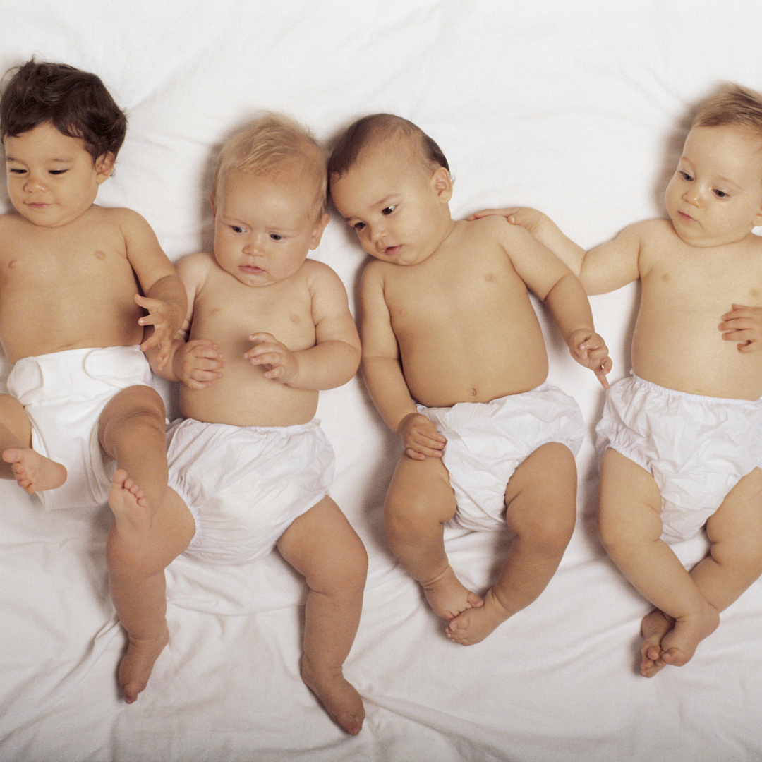 Four babies in nappies lying next to each other on a bed