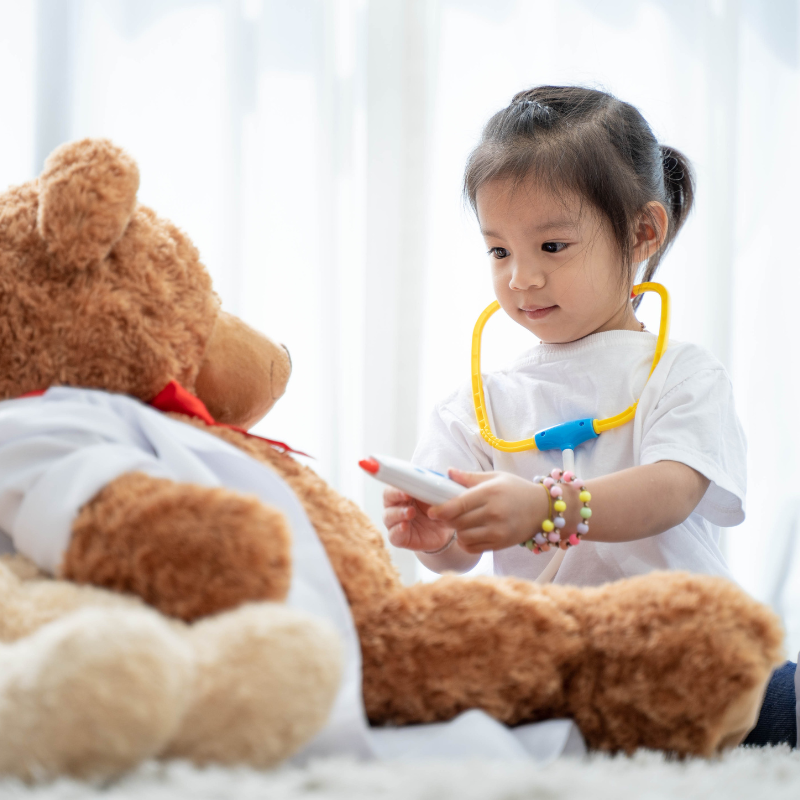 Toddler playing doctor with a big teddy bear